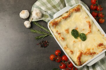 Delicious spinach lasagna in baking dish and ingredients on grey table, flat lay. Space for text