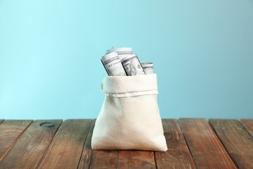 Dollar banknotes in burlap sack on wooden table against light blue background