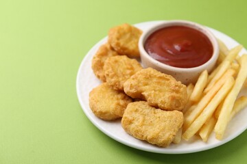 Tasty chicken nuggets and french fries with sauce on green background, closeup. Space for text