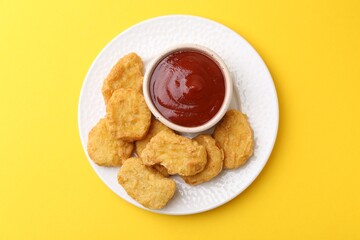 Tasty chicken nuggets with sauce on yellow background, top view
