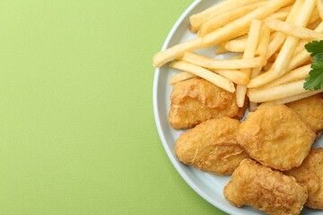 Tasty chicken nuggets and french fries on green background. Space for text
