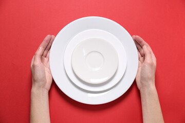 Woman holding ceramic plates on red background, top view