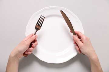 Woman with cutlery and empty plate at light table, top view