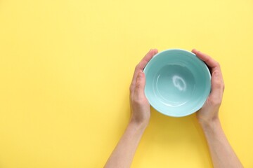 Woman holding ceramic bowl on yellow background, top view. Space for text