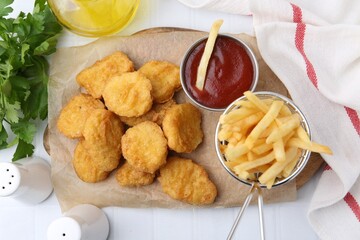 Tasty chicken nuggets, potato fries and ketchup on white tiled table, flat lay