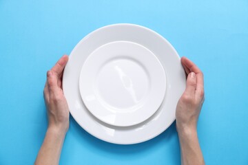 Woman holding ceramic plates on light blue background, top view