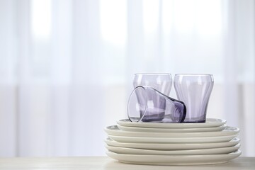 Empty clean glasses and plates on table indoors, space for text