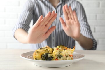 Woman refusing to eat piece of casserole at table, closeup