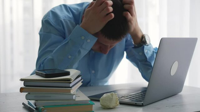 A tired man in a light-colored robe holds his head with his hands.
Exhaustion from work.
The man is tired at work.
A person is stressed from work.
Weakness and stress in a businessman.