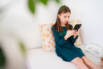 Young Girl Playing on a Handheld Gaming Console While Sitting on a Bed