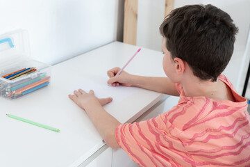 Young boy drawing at a white table with school supplies