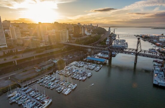 Aerial view of Tacoma waterfront at sunset. Many boats are docked in the marina, and a bridge spans the water. City skyline in the background. Foss Waterway, Tacoma Harbor, Washington, USA