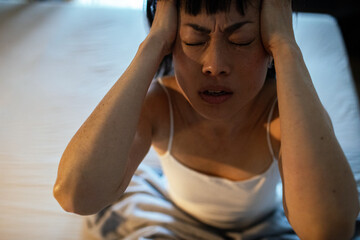 Asian woman experiencing headache or stress sitting on bed at night