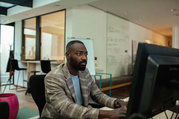 Black businessman working at desk with dual monitors in modern office