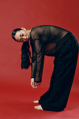 Fashion asian woman wearing a sheer top and black pants, bending over on a red background with hands on knees and feet on the ground