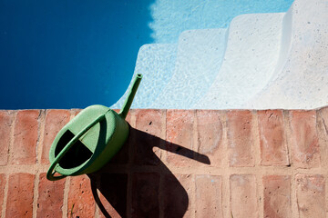 Refill swimming pool with watering can.  Concept for swimming pool service automation