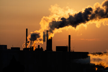 Silhouettes of factory pipe, chimneys at orange sunset with exhaust smoke, steam. Concept ecology, pollution, industry, smog, global warming.