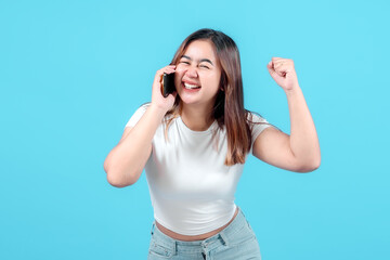 Fototapeta premium A cheerful young woman celebrates while talking on her smartphone, expressing joy and excitement against a bright blue background