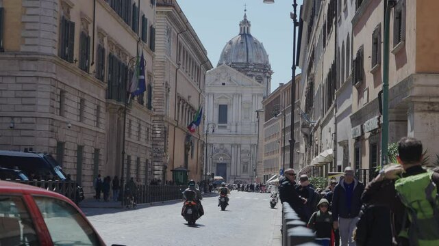 Lifestyle scene of bustling roman street with bikes driving and basilica Sant Andrea Della Valle at the end