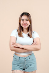 A confident young woman smiling with her arms crossed, showcasing a relaxed demeanor against a soft beige background, radiating positivity and self-assurance.