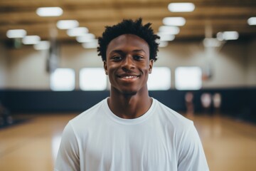 Obraz premium Smiling portrait of a young male African American basketball player wearing a white t shirt in an indoor basketball gym