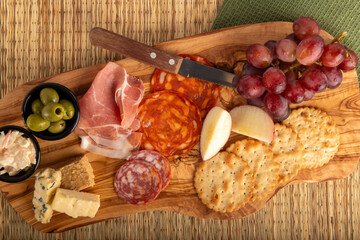 A wooden board top down zoomed in with a variety of food items including cheese, crackers, grapes, and meat