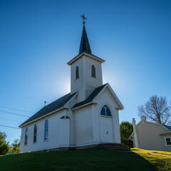 Fototapeta premium Beautiful white church with a tall steeple illuminated by golden sunset light, creating a peaceful and serene rural landscape