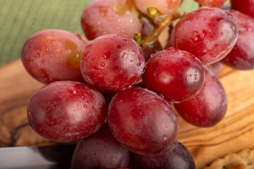 A bunch of grapes are wet and sitting on a wooden cutting board. The grapes are red and shiny, and they are arranged in a cluster. Concept of freshness and abundance, as the grapes are ripe