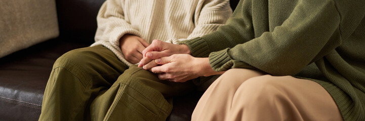 Header image of mother and daughter holding hands while sitting on couch during family therapy session close up