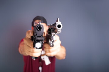 Studio portrait of a shooting instructor wearing a hat pointing two guns at the camera. Isolated on gray background. Sport practice.