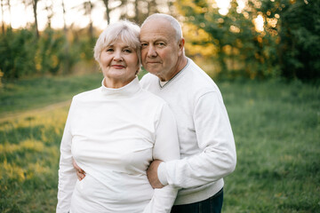a nice couple of grandparents who look good and pose for a photo in light clothes in front of a park