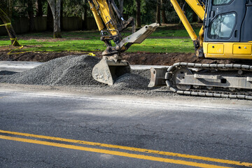 New public works sidewalk construction project between road and park, heavy equipment excavator...