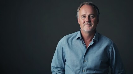 Fototapeta premium Confident Middle-Aged Man in Casual Blue Shirt Against Dark Background