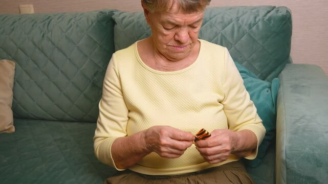 An elderly woman holds a St. George ribbon in her hands and pins it on her chest. The St. George ribbon is a symbol of May 9, the Victory Day of Russia in 1945