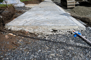 New public works sidewalk construction project, end of freshly poured concrete leading to gravel in...