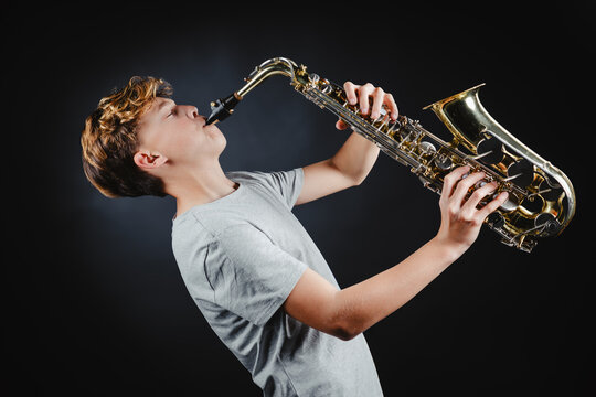 Teenage boy playing saxophone against dark background