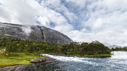 Obraz premium Breathtaking Natural Landscape: Majestic Mountains, Lush Forest, and Serene River Under a Cloudy Sky in Stunning Outdoor Adventure Scene