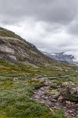 Breathtaking View of a Serene River Valley Surrounded by Majestic Mountains Under a Dramatic Cloudy Sky Captured in Scenic Nature Landscape