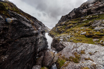 Breathtaking Mountain Scene Featuring Rugged Terrain, Stream, and Overcast Sky Captured in Majestic Landscape View with Dramatic Rock Formations and Lush Greenery