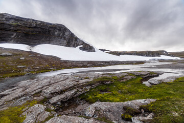 Stunning Landscape of Rocky Terrain with Snow-Capped Peaks and Flowing Water in a Serene Natural Environment Under Overcast Skies