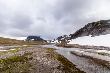A Scenic Landscape of Snow-Capped Mountains and a Tranquil River Flowing Through Rugged Terrain Under Cloudy Skies in Sweden's Remote Wilderness