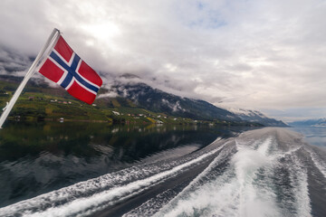 Stunning View of Norwegian Fjord with the Flag Flapping in the Breeze Amidst Cloudy Skies and Serene Reflection on Water Invoking the Beauty of Nature's Splendor and Tranquility