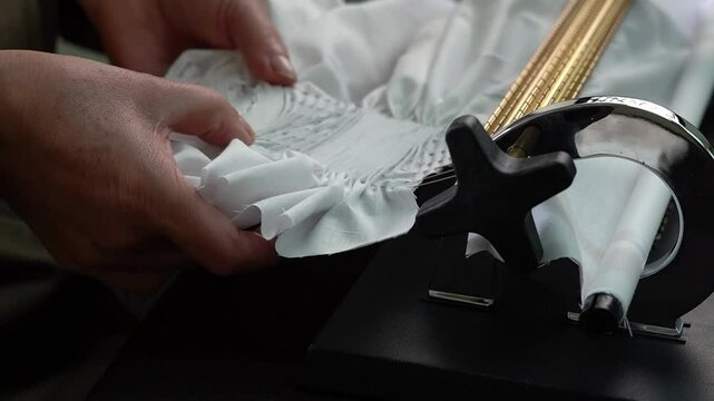 Close-up of hands using pucker machine to gather white fabric for smocking decoration