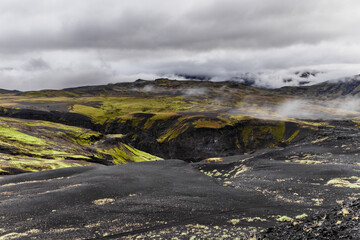 Stunning Contrast of Earth and Sky: A Beautiful Icelandic Landscape with Greenery, Dark Lava Fields, and Misty Clouds Capturing Nature's Unique Features and Colors