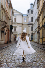 Obraz premium Stylish Woman in a White Coat Walking Through Cobblestone Streets