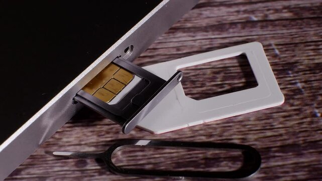 Closeup shot showing the sim card slot of a silver colored smartphone. The tool needed to open it. Communication. Modern technology. Wood background. Camera slowly moving around.