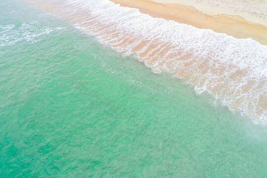 Turquoise water sea waves kissing the white sand in a tropical beach paradise, aerial drone directly above view