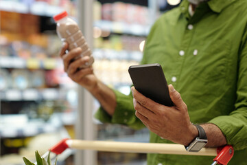 Close up of unrecognizable adult man using smartphone in supermarket while checking ingredients...