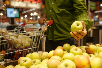 Closeup of unrecognizable man taking fresh ripe apple in fruits aisle at supermarket while doing grocery shopping, copy space
