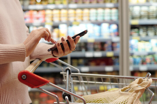 Side view close up of woman shopping in supermarket and using smartphone, copy space